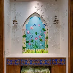 I love bringing artistic visions to life, like in this ornate niche mandir. The design features a hand-painted panel of lotuses and birds set within a traditional arch, complemented by intricate blue and gold drawers. The surrounding walls are adorned with 3D floral carvings, and classic hanging brass bells complete the temple-like feel, making it a truly bespoke piece of art.