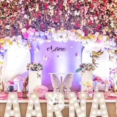 The main stage for this butterfly fairy party was a breathtaking sight, with a ceiling covered in flowers and a backdrop of soft purples and pinks. The large, illuminated marquee letters spelling "AARNA" added a personalized, high-impact touch.