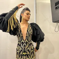 A backstage moment capturing the full effect of this high-fashion look. The sleek ponytail and dramatic makeup were designed to complement the structured, avant-garde gown.