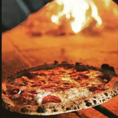 A classic pepperoni pizza baking next to the open flames. This shot captures the intense heat of the wood-fired oven, which is the secret to a quick bake and an incredible crust.