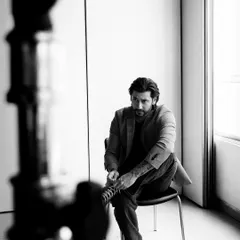 A candid, behind-the-scenes style black and white shot. The framing with the light stand adds a cool, industrial-chic element.