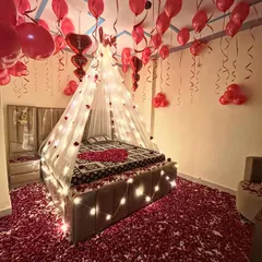 A full view of the romantic bedroom setup, showing the 'I Love You' balloons and the heart made of petals on the bed.