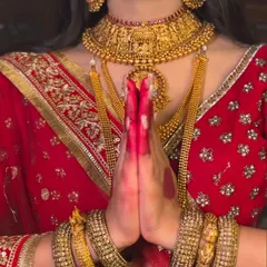 A close-up shot focusing on the traditional elements of the Padmavati look. The hands are held in a namaste gesture, adorned with alta and heavy gold bangles, with the temple necklace visible.