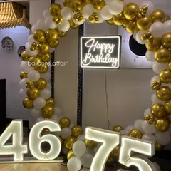 A grand double birthday celebration with a gold and white theme. This setup features a large circular balloon arch and marquee numbers for ages 46 and 75.