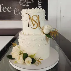 This sophisticated two-tiered wedding cake is decorated with edible pearls and a custom gold acrylic "MS" monogram. Fresh white roses and gold leaves complete this elegant design.