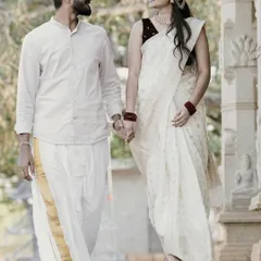A beautiful shot of a couple in matching white and gold traditional outfits, walking hand-in-hand at a temple-themed location, perfect for a cultural pre-wedding session.