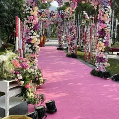 A vibrant pink floral carpet leads the way down this stunning outdoor aisle. The path is lined with lush, multi-colored floral arches, creating a joyful and celebratory entrance for a garden wedding.