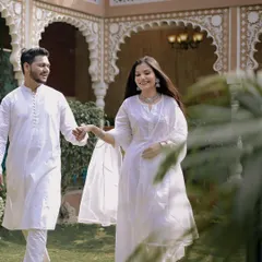 A happy, candid moment of the couple walking through the gardens of a heritage-style venue. Their coordinated white outfits create a look of pure elegance for this pre-wedding shoot.