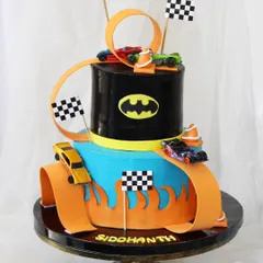 A dream cake for a Hot Wheels fan. This two-tiered design features a winding orange track with real Hot Wheels cars racing around a Batman-themed tier, complete with checkered flags for a thrilling finish.