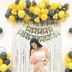 A classic birthday photo backdrop for home parties. This setup includes a silver shimmer curtain, a 'Happy Birthday' banner, and a yellow and black balloon arrangement.