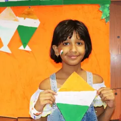 A girl with a tricolor painted on her cheek shows off her handmade kite. Face painting and themed crafts are some of the most popular activities during our festive events.