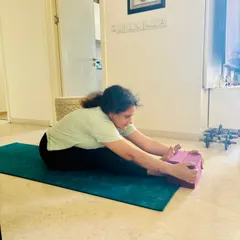 A closer look at the student's form in the supported forward bend. Notice how the blocks help her extend her spine and reach further without rounding her back, ensuring a safe and effective hamstring stretch.