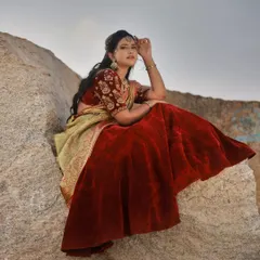 A seated portrait on a large boulder. The soft, natural light of the evening sky complements the rich red velvet of the lehenga and the intricate ethnic jewellery.
