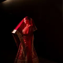 A bride in a regal red lehenga, captured in a dramatic play of light and shadow. This portrait highlights her elegance and the rich color of her attire, creating a powerful and timeless image.