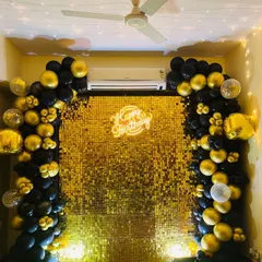 A glamorous birthday setup with a full gold sequin wall. The balloon arch in black and gold chrome adds a touch of luxury, perfect for a milestone celebration.