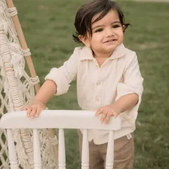 A sweet toddler portrait taken during an outdoor session, with a boho-style chair as a prop.