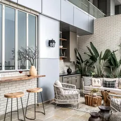 This deck features a versatile wooden ledge adjacent to the kitchen, serving as both a serving table and a high bar. The deck walls are clad in white bricks, infusing a distinctive urban modern farmhouse style.