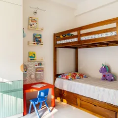 In this kids' room, versatility is key. A trundle-cum-bunk bed is perfect for sleepovers, while the wardrobe, painted in a soft green, keeps the space feeling light and airy. A small red table and blue chair add a primary color pop for a play area.