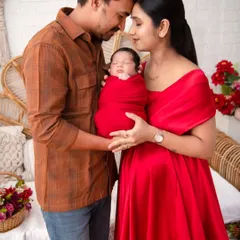 A newborn wrapped in red, held lovingly by his parents. This intimate portrait captures the warmth and protective embrace of new parenthood against a soft, rustic backdrop.