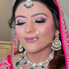 A close-up of a stunning bridal makeup look. The focus is on the intricate smokey eye with shades of pink and purple, paired with a matte pink lip and glowing skin, perfectly complementing her green and pink jewelry.