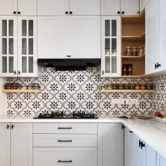 This kitchen has a classic, timeless feel with its white shaker-style cabinets and black hardware. The monochrome floral-patterned backsplash adds a touch of personality, and open wooden shelves provide easy access to spices.