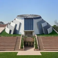 A frontal view of the completed museum building, showing its powerful, sculptural form rising from the landscape. The design features grand stairs leading to the entrance, creating a formal and welcoming approach.