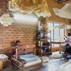 The interior of the Oorjasi paper-making workshop. The space is a hive of activity, with high ceilings and large windows providing ample light for the artisans at work. The exposed brick walls add to the studio's rustic, creative character.