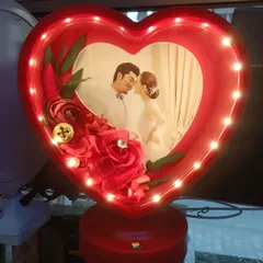 A close-up of our red heart-shaped 3D LED lamp. The photo is surrounded by beautiful artificial roses, and the entire frame lights up to create a romantic glow.