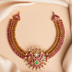 This unique choker is crafted with a flexible, woven gold-toned metal base, lined with vibrant pink stones. The centerpiece is a circular, sun-like motif with intricate detailing, making it a bold and artistic choice.