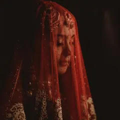 A dramatic, veiled portrait of the bride. The sheer red dupatta with delicate embroidery creates a sense of mystery and timeless romance.