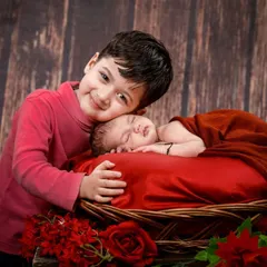 A classic sibling portrait with an older brother lovingly watching over his sleeping newborn brother in a basket. The rich, warm tones create a timeless feel.