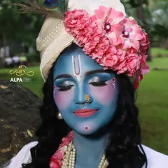 A close-up of the Krishna makeup. The look features a smooth blue base, serene eye makeup, and a floral-adorned turban with a peacock feather.