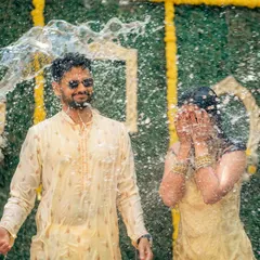 The Haldi ceremony is all about unrestrained joy. I love capturing these candid, fun-filled moments, like this one where the couple is showered with water against a vibrant backdrop of marigolds and a custom green wall.