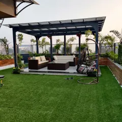 A complete terrace transformation for a home, featuring a custom pergola for shade, a comfortable outdoor sofa set, a swing chair, and durable artificial grass for a low-maintenance lawn.