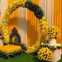 A modern Haldi decor featuring a floral ring of yellow marigolds against a backdrop of yellow and white striped curtains.