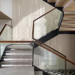 A staircase is more than just a connection between floors; it is the spine of the home. This sculptural piece combines the lightness of glass with the warmth of wood, set against fluted wall panels and geometric marble flooring. We design these transitional moments to be an experience of architectural beauty and grace.