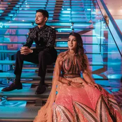 A stylish portrait of the couple seated on a modern, illuminated staircase, capturing a moment of cool composure amidst their vibrant reception.