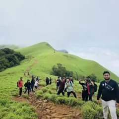 A wide shot of our group on a narrow trail winding through the rolling green hills of Kudremukha. This shows the epic scale of the landscapes we explore on our weekend treks.