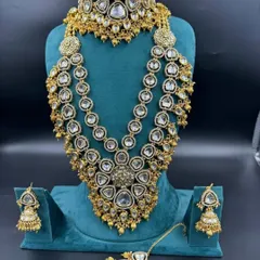This is one of our grandest bridal sets, perfect for making a statement. It features multiple layers of American diamonds and Kundan work, including a heavy choker, a three-layer rani haar, matching jhumkas, and a maang tikka. It gives you a luxurious designer look at an affordable rental price.