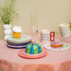 A playful and colorful tableware setup on a pink tablecloth. This shot showcases a variety of quirky, handmade ceramic pieces, including a butter dish, mugs, and plates.