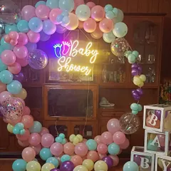 A beautiful baby shower setup with a pastel-colored balloon ring. The "Baby Shower" neon sign and "BABY" blocks make for a perfect photo corner.