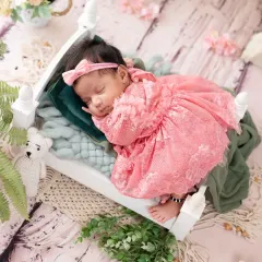 A sleeping newborn princess in a frilly pink lace dress, resting on a tiny white bed.