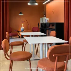 This cafe interior is designed to be a cozy retreat for customers. The warm terracotta color scheme, comfortable seating, and modern lighting create a perfect ambiance for a coffee shop.