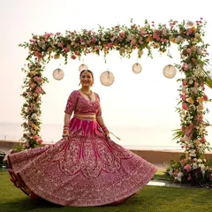 The bride twirls in her vibrant pink lehenga, creating a beautiful motion shot against the beachside floral mandap. A moment of pure bridal joy.