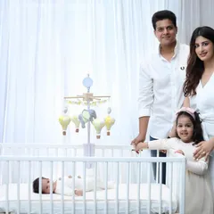 A beautiful family portrait taken in the nursery. The family stands together by the crib, smiling for a picture that feels both composed and wonderfully natural.