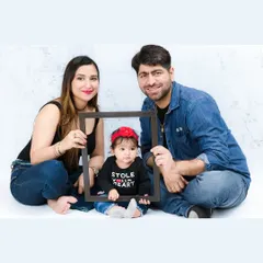 A creative family portrait where the parents hold a frame around their adorable baby, who is wearing a "Stole Your Heart" t-shirt. It's a fun and modern take on the family photo.