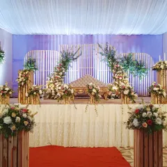 This is a modern rustic stage design with white slatted back panels and asymmetrical floral arches. The arrangement uses plenty of green foliage and white flowers for a fresh, contemporary look.