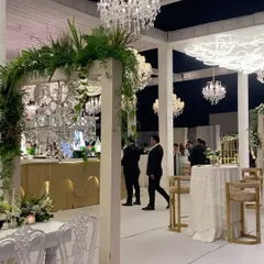 A stylish bar area that is both functional and beautiful. The custom white and gold bar is framed by a greenery-clad arch, with elegant high-top tables providing a chic space for guests to mingle.