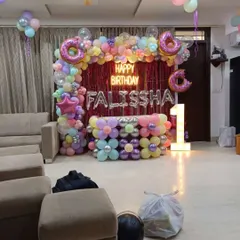 A sweet and colorful donut-themed first birthday. The backdrop is a pink tinsel curtain with a balloon arch featuring pastel colors and large donut-shaped foil balloons.
