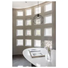 Light filters through the grid of windows in the 'House Under Tabebuia Trees', creating a serene atmosphere at the curved dining table. The industrial-style pendant light adds a modern touch.